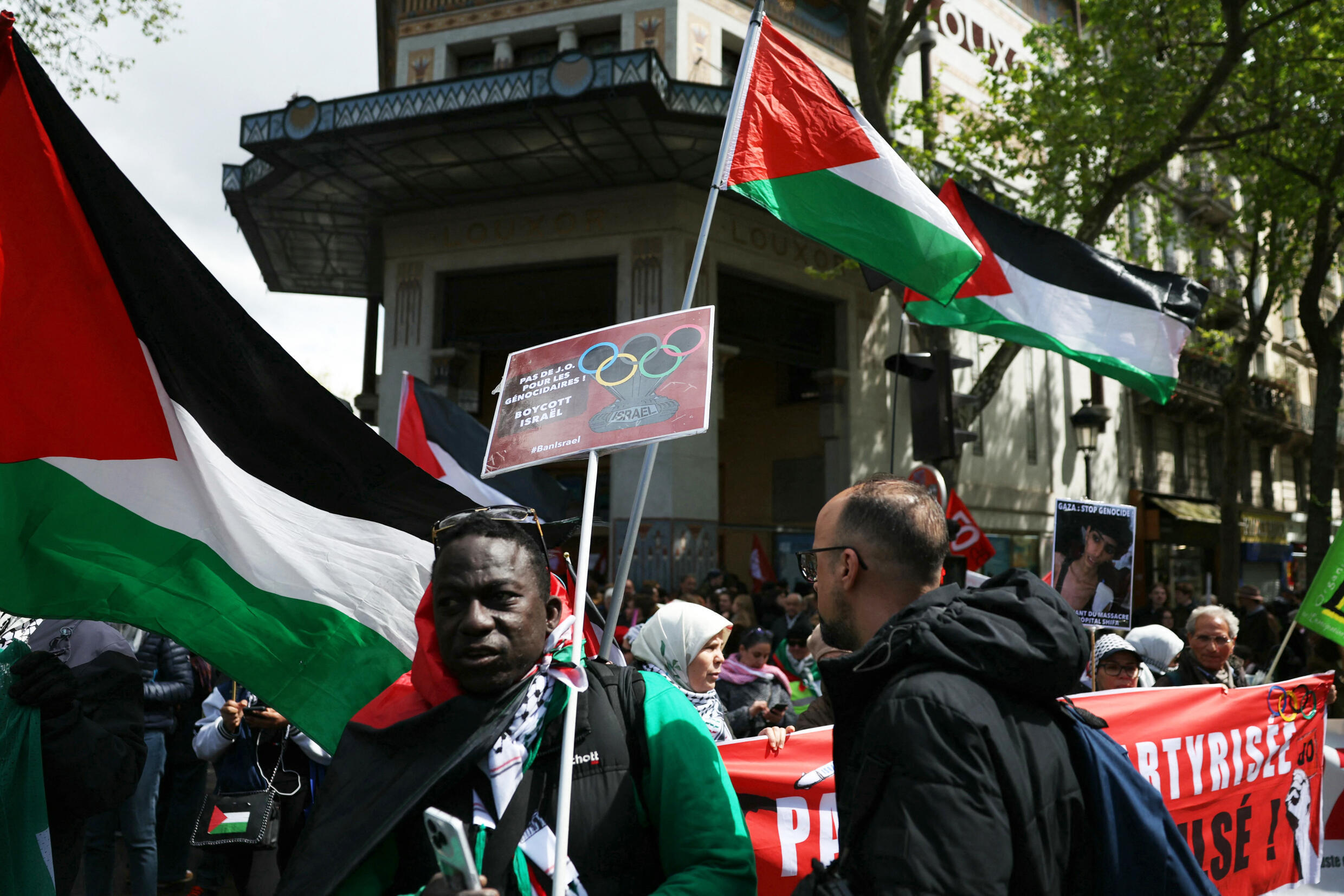 Des manifestants brandissent des drapeaux palestiniens et une pancarte indiquant « Pas de Jeux olympiques pour les auteurs du génocide, boycottez Israël » lors d'une manifestation « contre le racisme, contre l'islamophobie » à l'appel de diverses organisations à Paris le 21 avril 2024.