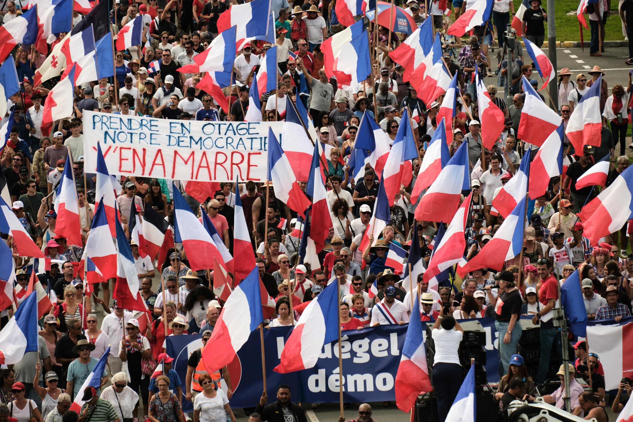 Des manifestants de plusieurs partis loyalistes brandissent des drapeaux nationaux français et brandissent une banderole "Prendre en otage notre démocrate y'en a marre" (Enlevez-vous notre démocratie) alors qu'ils défilent lors d'une manifestation en faveur de l'élargissement du corps électoral pour les prochaines élections provinciales en Nouvelle-Calédonie, à Nouméa, le 13 avril 2024.
