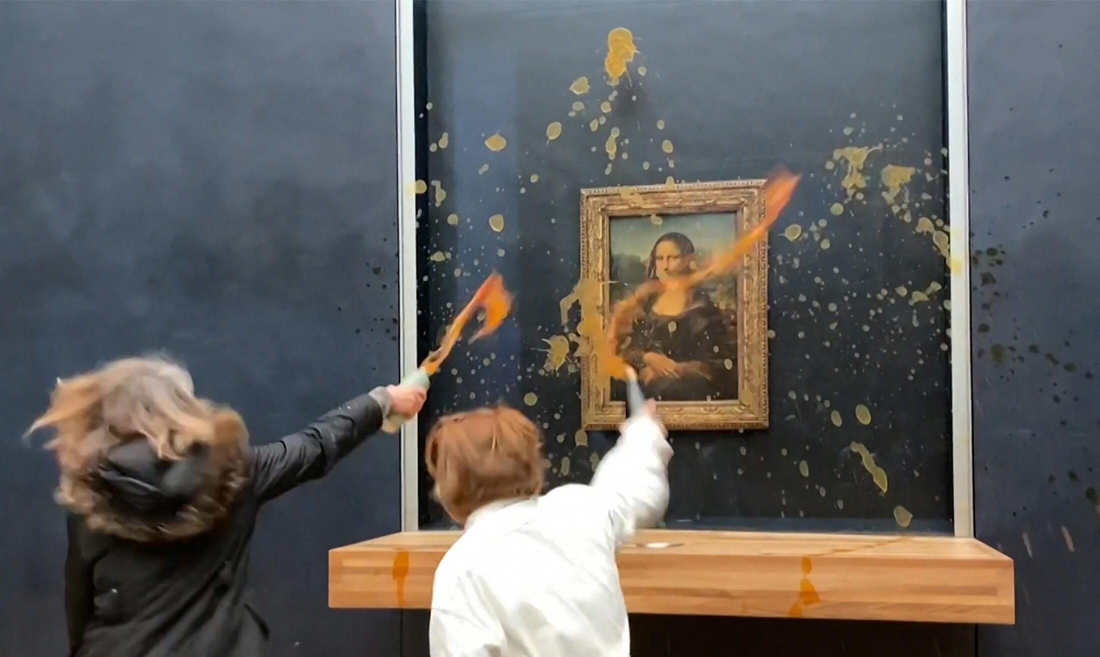 Cette image extraite d'une séquence de l'AFPTV montre deux militants écologistes du collectif adoubé "Riposte Alimentaire" (Représailles alimentaires) lançant de la soupe chez Léonard de Vinci "Mona Lisa" (La Joconde), au musée du Louvre à Paris, le 28 janvier 2024.