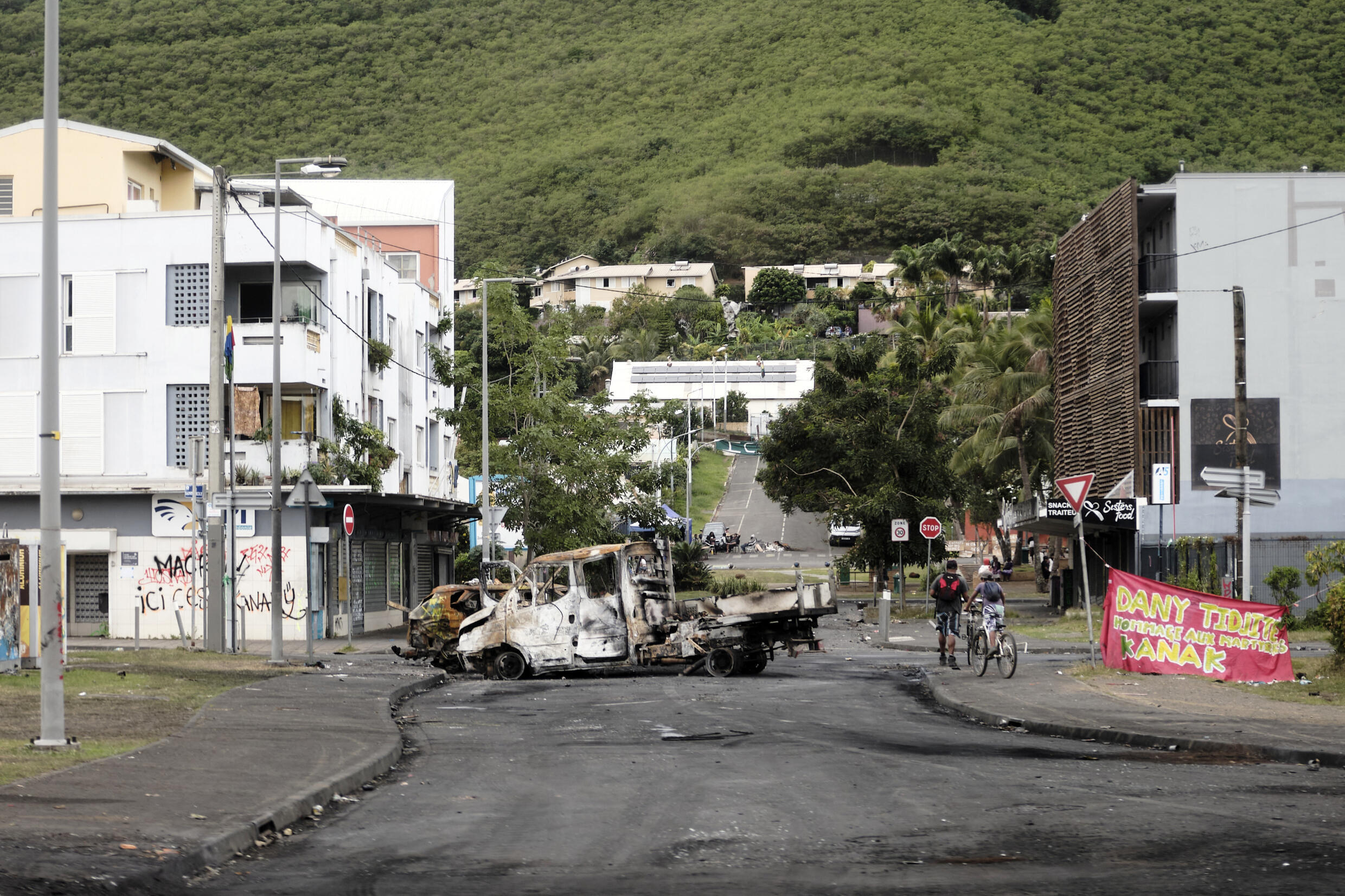Un enfant passe à vélo devant des voitures incendiées dans le quartier de La vallée du Tir, où la circulation n'a pas encore été rétablie par les autorités, l'accès aux soins, à la nourriture et à l'essence restant précaire, à Nouméa, en Nouvelle-Calédonie, le 28 mai 2024.