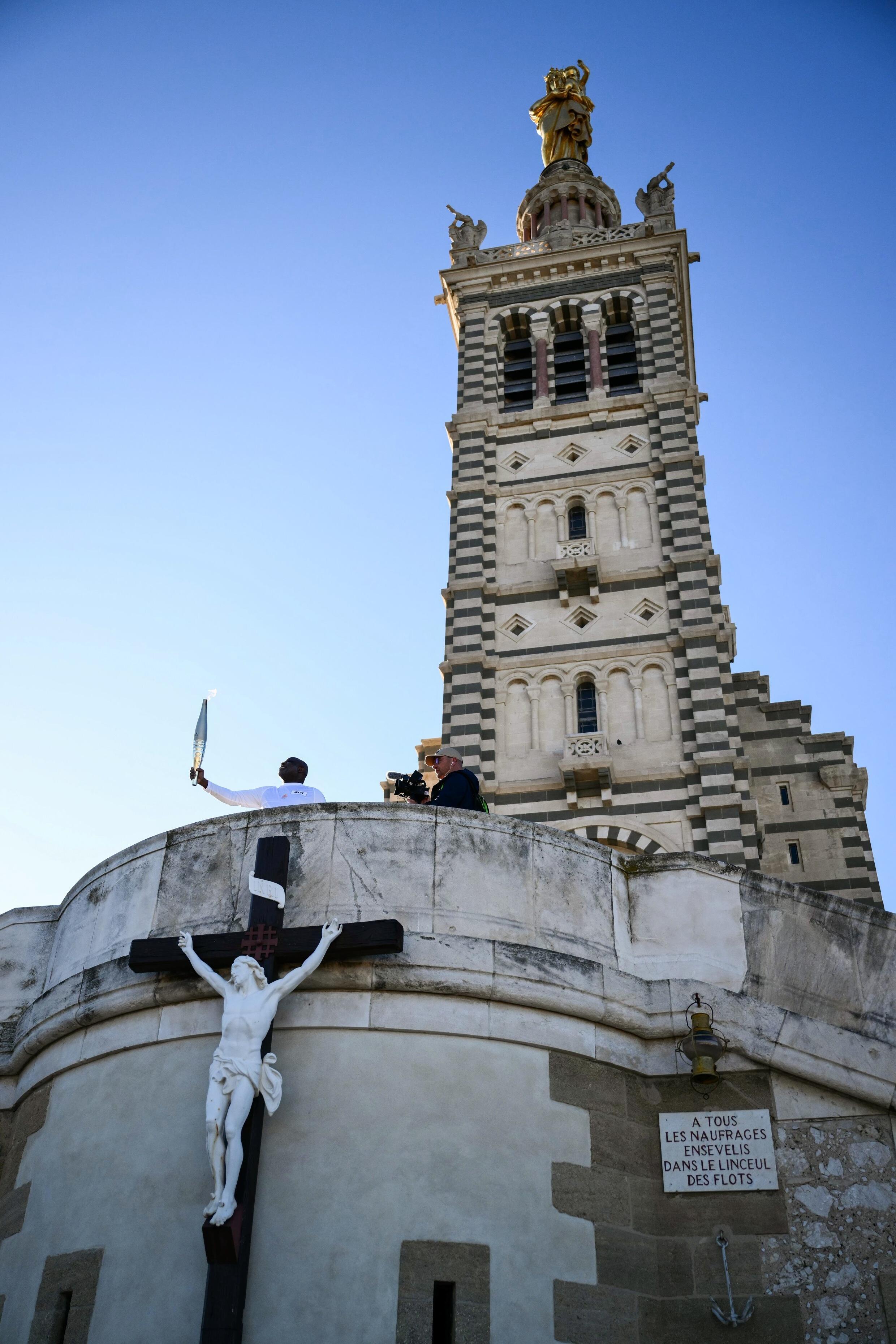 Basile Boli brandit la flamme olympique devant la basilique Notre-Dame de la Garde à Marseille