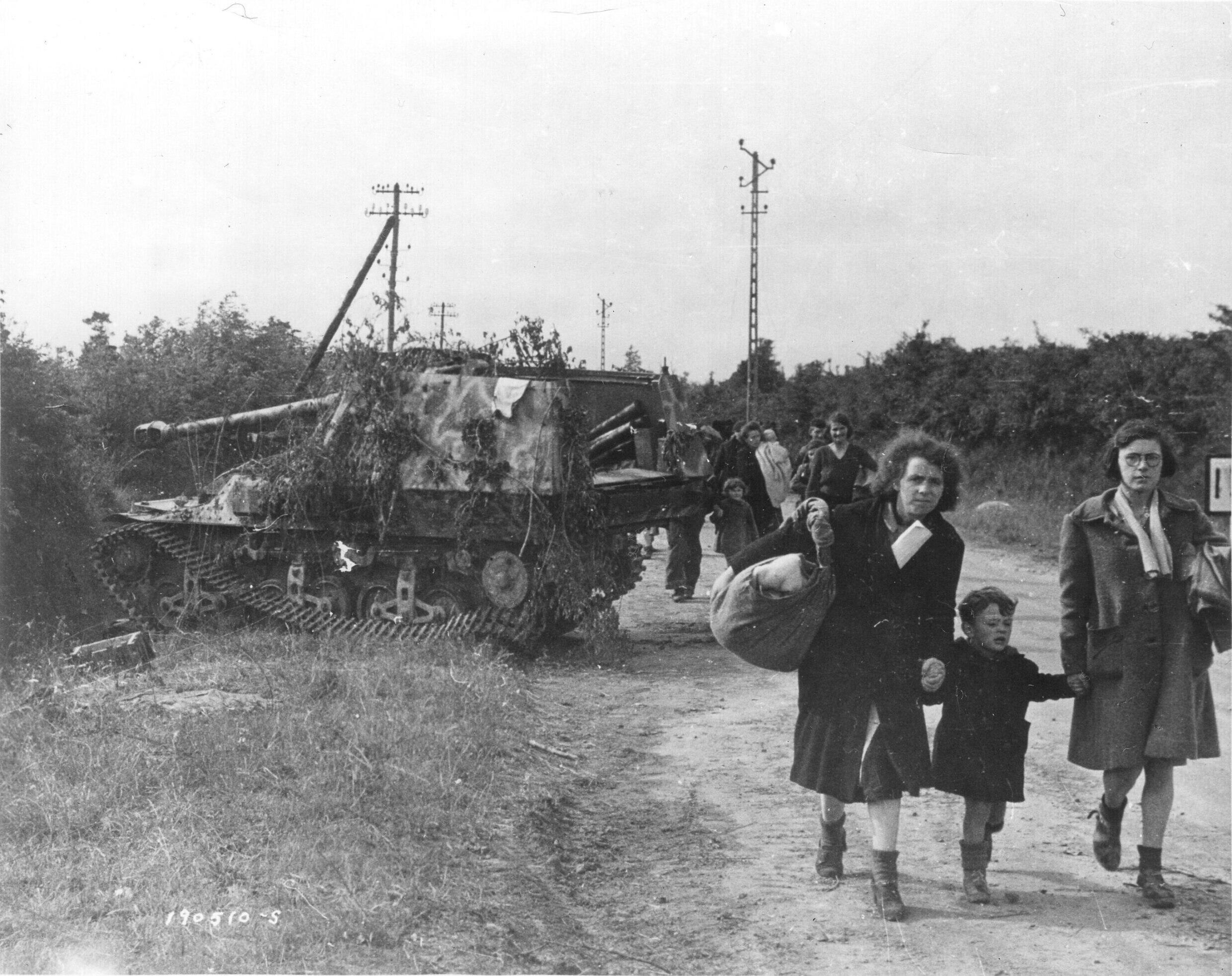 Des réfugiés français défilent devant un char allemand détruit alors qu'ils fuient pour échapper aux combats entre forces alliées et nazies, le 21 juin 1944.