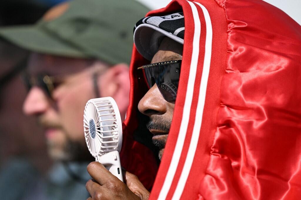 Le rappeur américain Snoop Dogg drape une veste autour de sa tête pour se protéger de la chaleur et tient un ventilateur de poche pour se rafraîchir pendant qu'il regarde la finale masculine de skateboard de rue à La Concorde à Paris le 29 juillet 2024.