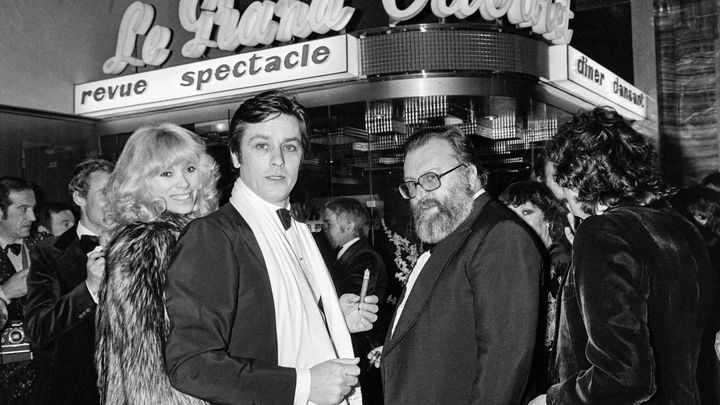 Alain Delon et Mireille Darc, en couple, avec le réalisateur Sergio Leone, lors de l'ouverture de la discothèque "Le Grand Cabaret", le 15 janvier 1977 à Nice. (AFP)